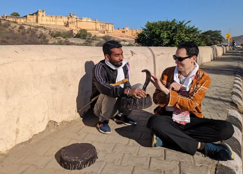 Adam pets a cobra with a snake charmer